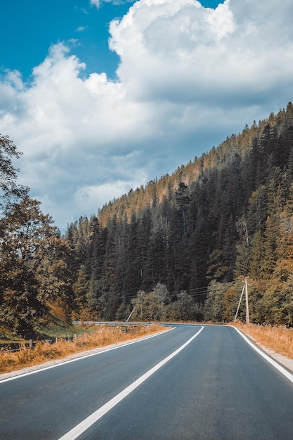 Disparo vertical de una carretera de asfalto vacía a través de montañas bajo un cielo nublado