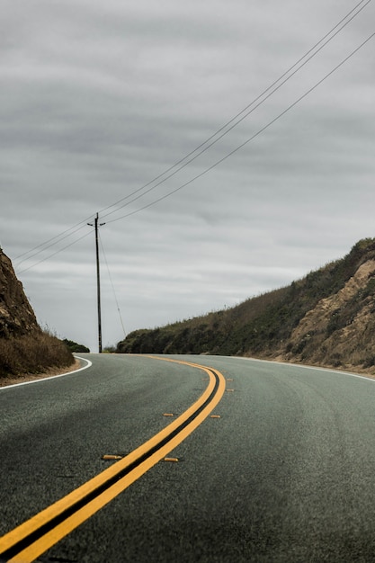 Foto gratuita disparo vertical de una carretera de dos lados rodeada de colinas con el nublado cielo gris en el