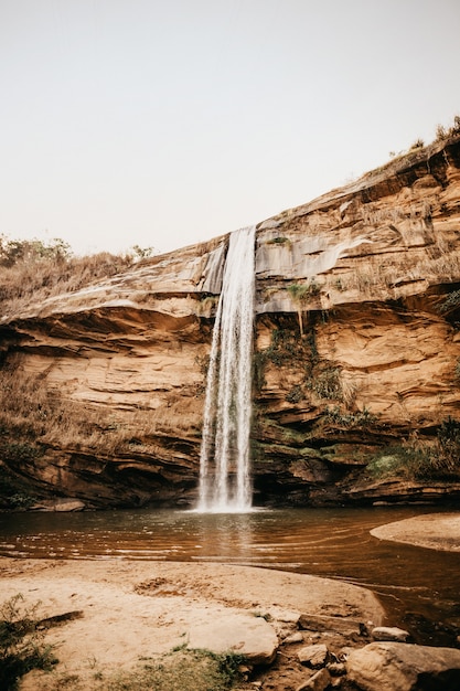 Disparo vertical de una cascada que fluye desde un acantilado bajo en un pequeño césped durante el día