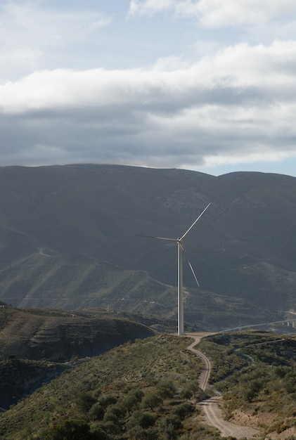 Disparo vertical de colinas cubiertas de vegetación con un molino de viento en el fondo bajo un cielo nublado