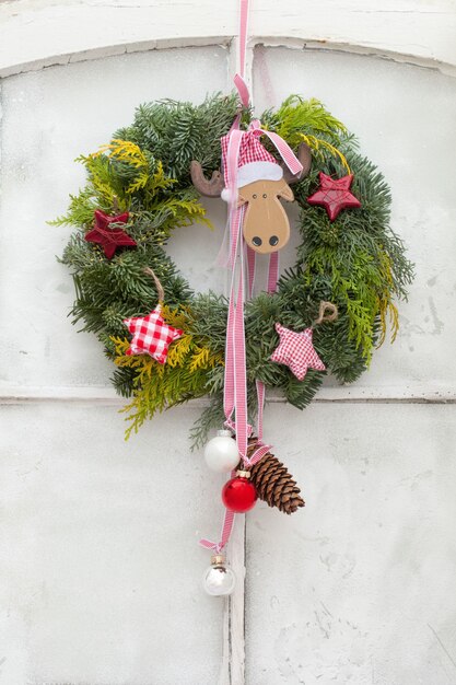 Disparo vertical de una corona de Navidad decorativa con adornos colgando de una puerta blanca