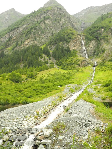 Disparo vertical de una corriente de agua rodeada de montañas verdes con un cielo sombrío