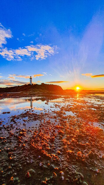 Disparo vertical de una costa con un faro al fondo durante la puesta de sol