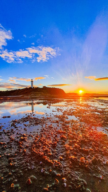 Disparo vertical de una costa con un faro al fondo durante la puesta de sol