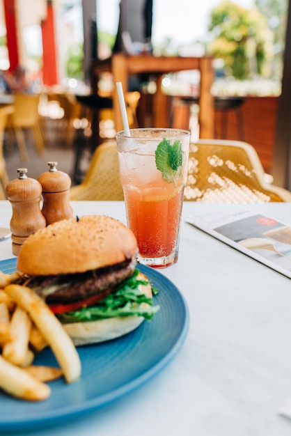 Disparo vertical de una deliciosa hamburguesa y unas papas fritas y una copa de cóctel en la mesa