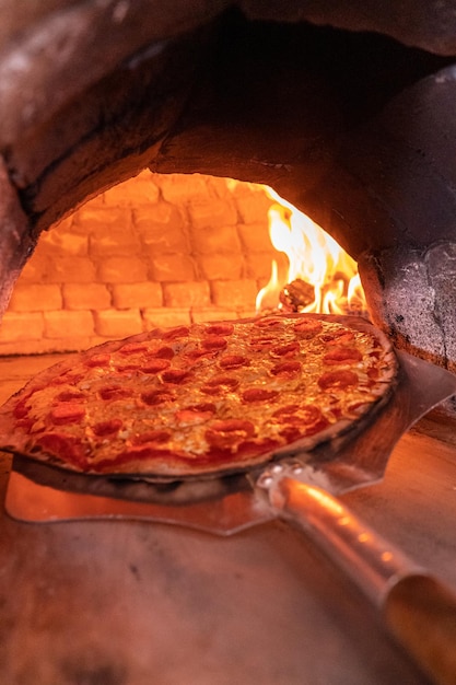 Disparo vertical de una deliciosa pizza de pepperoni cursi dentro del horno de piedra de ladrillo