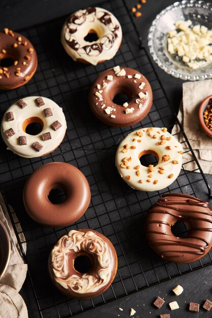 Disparo vertical de deliciosas donas cubiertas con el glaseado de chocolate blanco y marrón sobre un cuadro negro