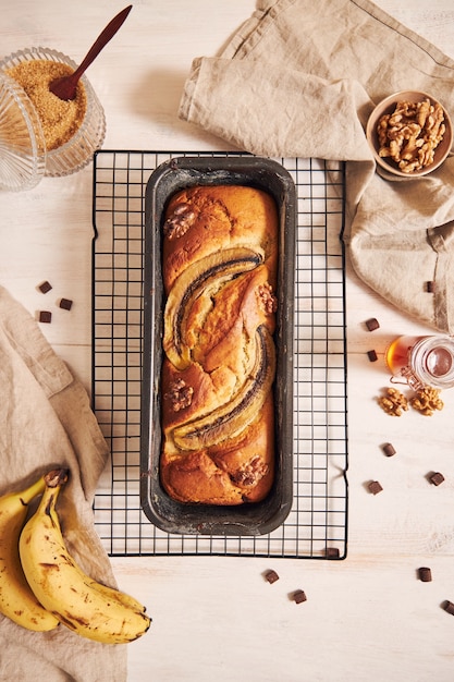 Disparo vertical de delicioso pan de plátano en un molde para pan con trozos de chocolate y nueces sobre una mesa