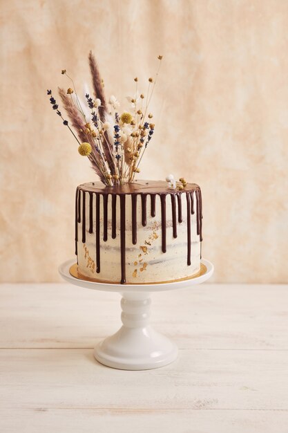 Disparo vertical de delicioso pastel Boho con goteo de chocolate y flores en la parte superior con adornos dorados