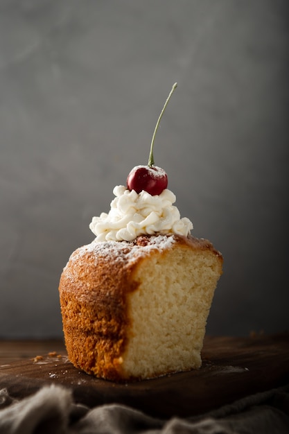 Disparo vertical de un delicioso pastel con crema, azúcar en polvo y una cereza en la parte superior