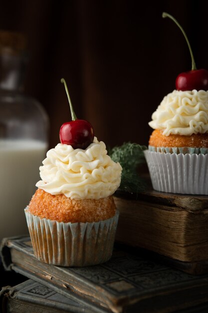 Disparo vertical de deliciosos cupcakes con crema y cerezas en la parte superior de los libros