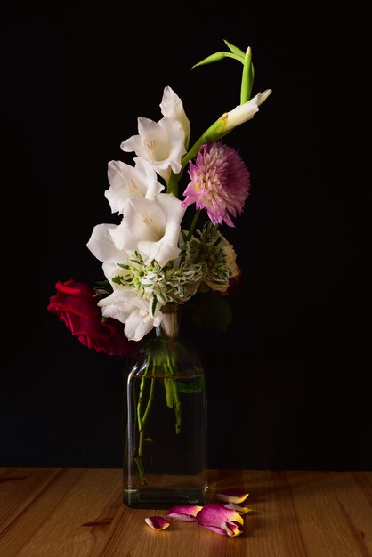 Disparo vertical de diferentes flores en un frasco sobre una superficie de madera con un fondo negro