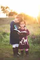 Foto gratuita disparo vertical de dos adorables hermanitas leyendo la biblia en el parque