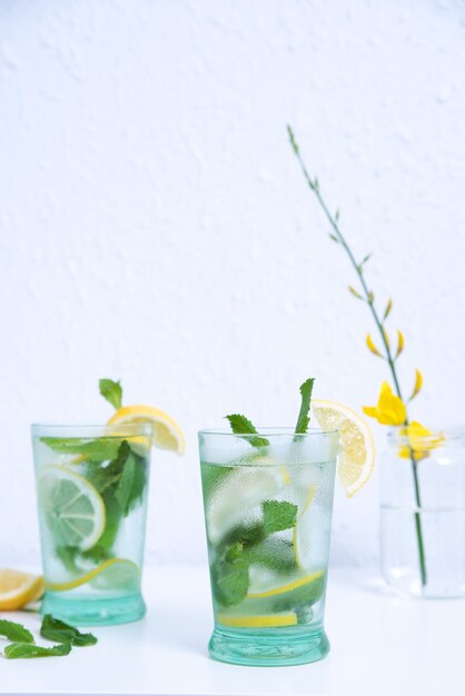 Disparo vertical de dos vasos de limonada fría con menta y limones aislado en una pared blanca