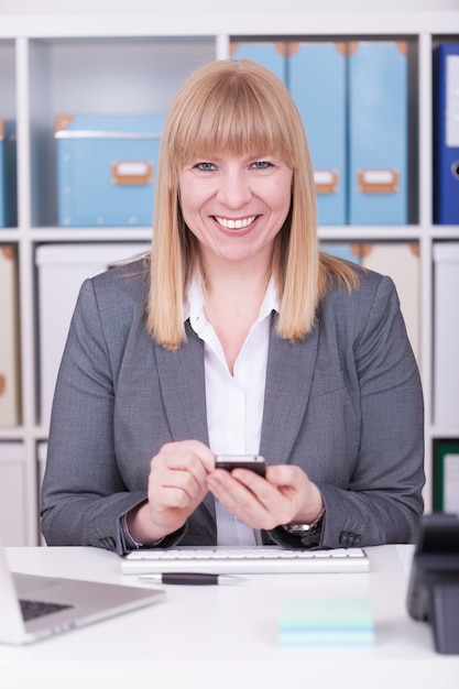 Disparo vertical de una empresaria caucásica feliz sosteniendo su teléfono y sonriendo