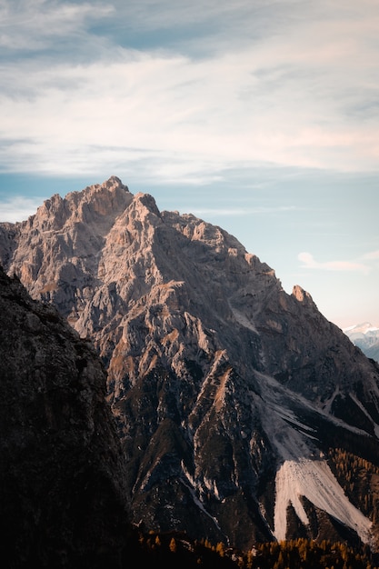 Disparo vertical de la escarpada montaña rocosa con un pico iluminado por el sol en la Cordillera de los Dolomitas, Italia
