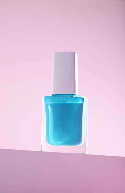 Disparo vertical de esmalte de uñas azul contra una pared rosa