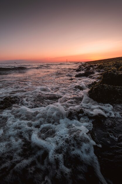 Disparo vertical de espumosas olas del mar llegando a la orilla con la increíble puesta de sol