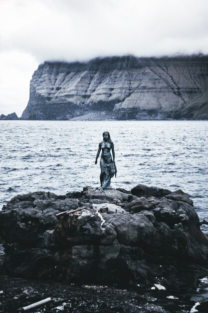 Un disparo vertical de una estatua femenina cerca del mar.