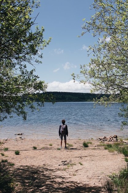 Disparo vertical de un excursionista de pie en la playa junto a un lago y las colinas en el fondo