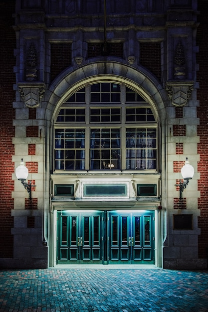 Foto gratuita disparo vertical de la fachada de un antiguo edificio gótico de ladrillo con lámparas encendidas, por la noche