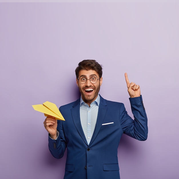 Disparo vertical de feliz director masculino en elegante ropa formal, señala el dedo índice arriba