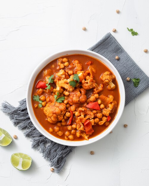 Disparo vertical de garbanzos al curry chana masala con limón en un recipiente sobre un surf blanco