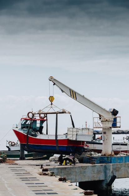 Disparo vertical de una grúa levantando un barco blanco en un muelle