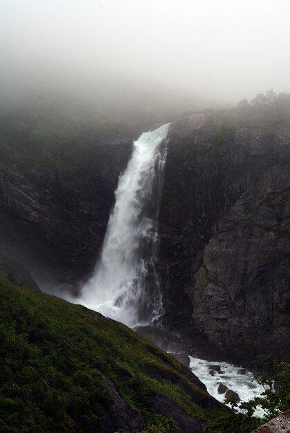 Disparo vertical de una hermosa cascada en las montañas envueltas con niebla en Noruega