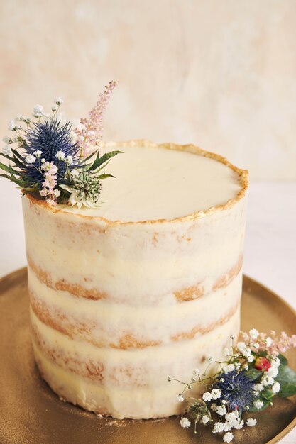 Disparo vertical de un hermoso y delicioso pastel con flores y bordes dorados sobre un fondo blanco.