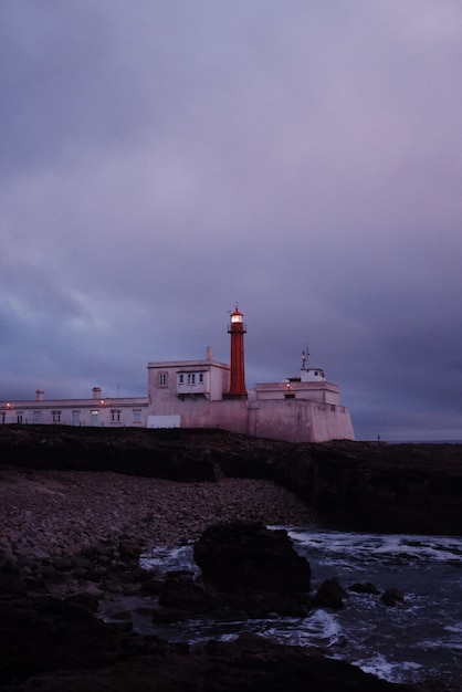 Disparo vertical de un hermoso paisaje del faro después del atardecer con cielo púrpura