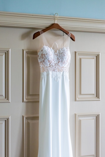 Disparo vertical de un hermoso vestido de novia blanco colgando de la puerta en la habitación de la novia
