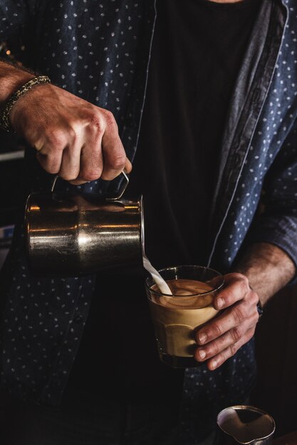 Disparo vertical de un hombre vertiendo leche en un vaso de café