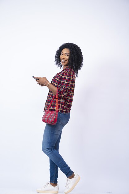 Disparo vertical de una joven africana feliz caminando de lado mientras usa su teléfono