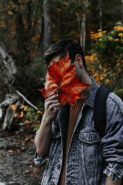 Disparo vertical de un joven macho que cubre toda su cara con una gran hoja dorada de otoño