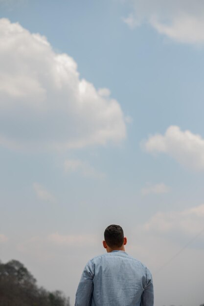 Disparo vertical de un joven mirando el cielo nublado azul