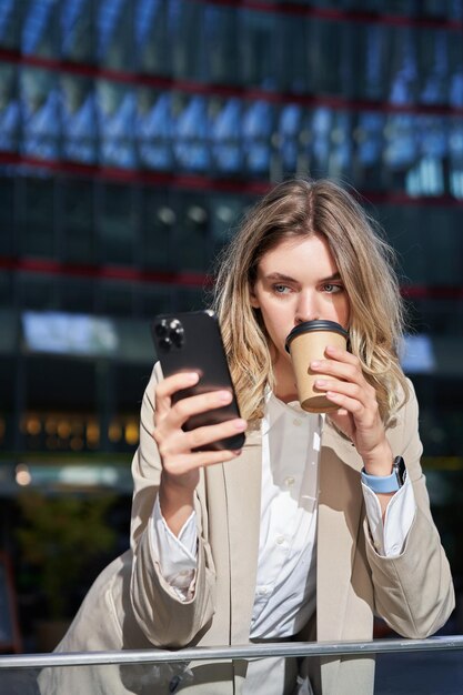 Disparo vertical de una joven mujer corporativa bebe su café y mira el mensaje de texto del teléfono móvil sta