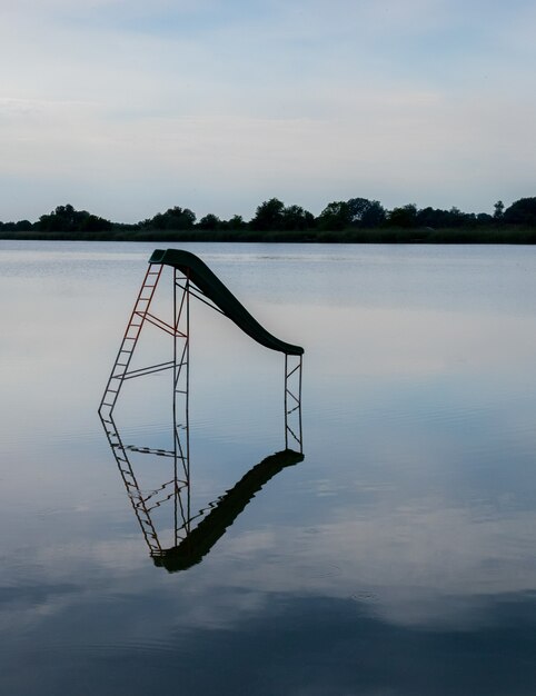 Disparo vertical de un lago con un columpio de agua reflejada en el agua y árboles en el fondo