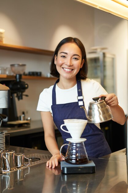 Disparo vertical de una linda estudiante de barista asiática que trabaja en una cafetería vertiendo agua en la cerveza de filtro