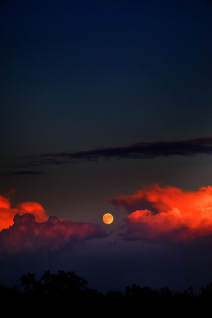 Disparo vertical de la luna y las nubes de fuego en el cielo oscuro