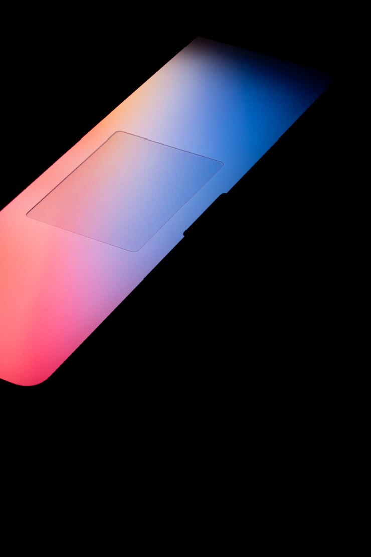 Foto gratuito disparo vertical de una luz de colores brillantes que sale de la pantalla de un portátil en la oscuridad