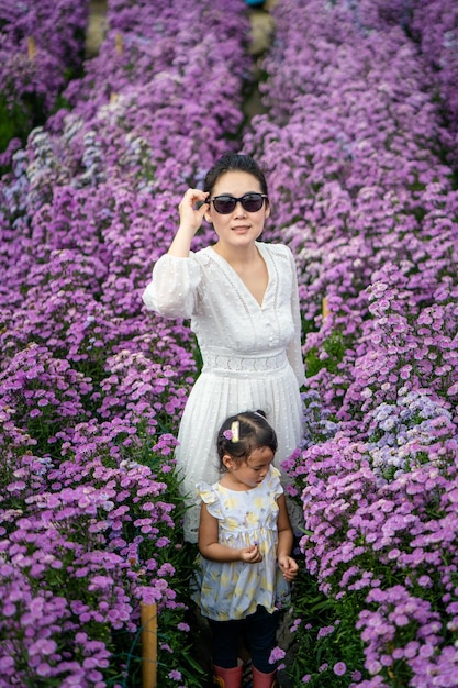 Disparo vertical de madre e hija tailandesas disfrutando de flores de ageratum púrpura en el campo