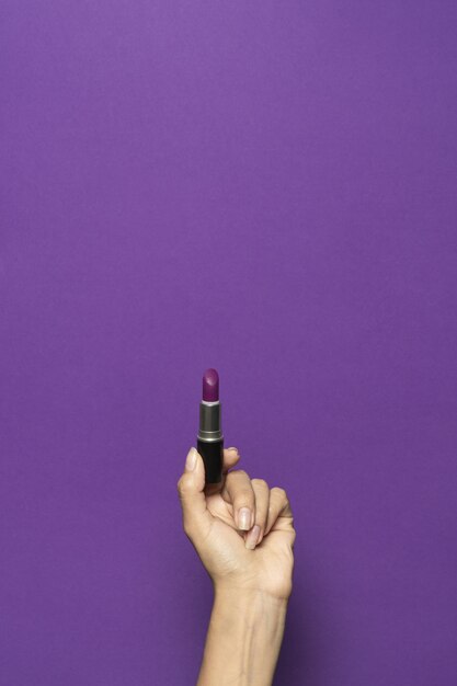Disparo vertical de una mano sosteniendo un lápiz labial aislado sobre un fondo violeta