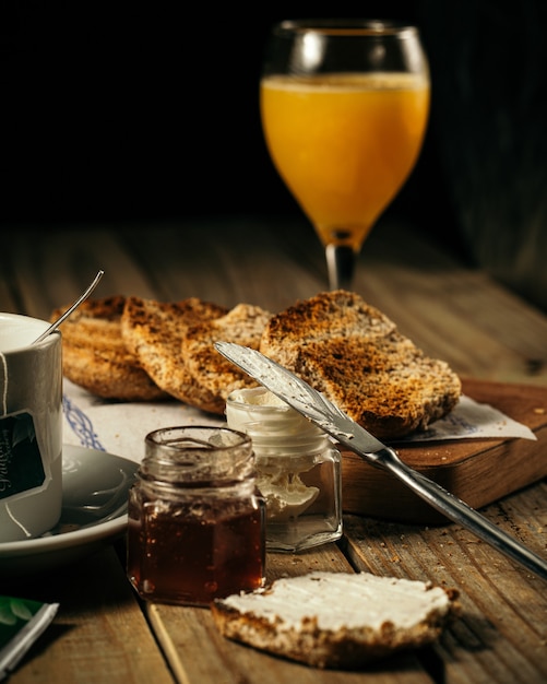 Disparo vertical de miel y jugo de naranja y un cuchillo para untar la crema sobre una rebanada de pan sobre una mesa