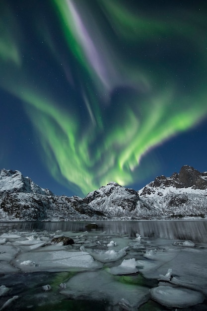 Un disparo vertical de montañas nevadas bajo una hermosa luz polar durante la noche