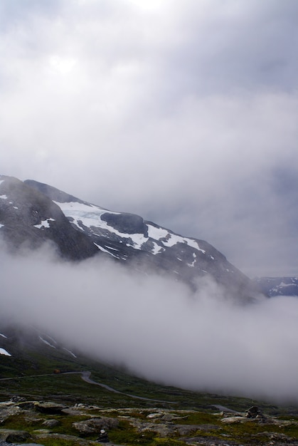 Disparo vertical de montañas rocosas cubiertas de nieve y niebla en Noruega