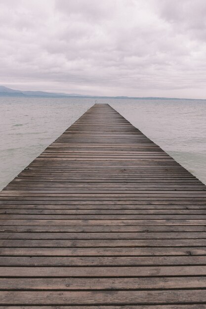 Foto gratuita disparo vertical de un muelle de madera sobre el océano tranquilo bajo el hermoso cielo nublado