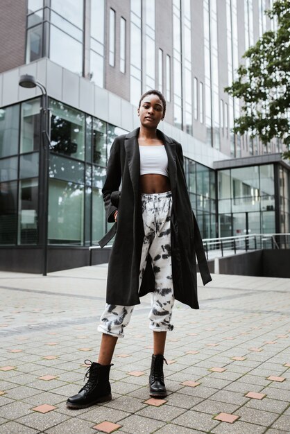 Disparo vertical de una mujer afroamericana con un abrigo posando en la calle