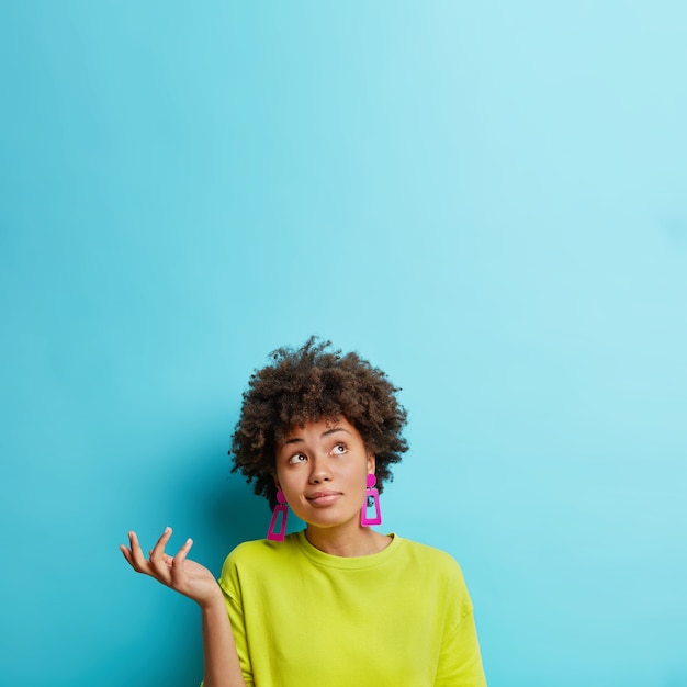 Foto gratuita disparo vertical de mujer afroamericana dudosa levanta la mano con duda parece confundido arriba toma decisión