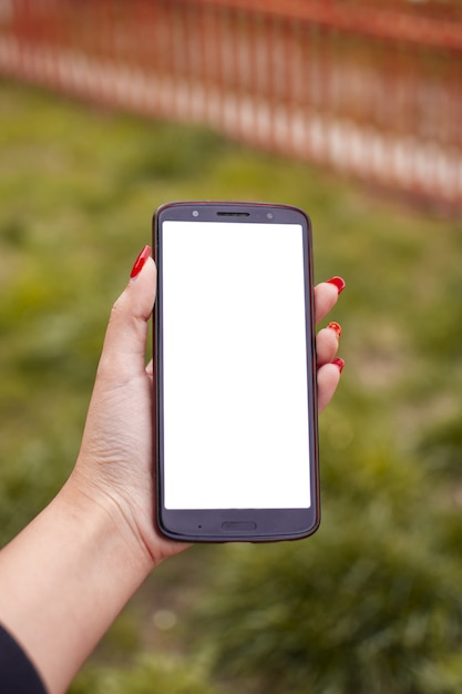 Disparo vertical de una mujer con esmalte de uñas rojo sosteniendo un teléfono con una pantalla en blanco